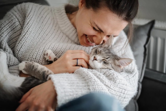 woman cuddling grey cat. Signs your cat loves you.